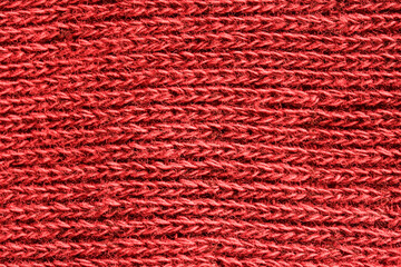 Cozy background or backdrop made of texture of red warm textile material. Cotton and wool. Fragment of a red Christmas sweater. Horizontal fibers. Photo. Macro.