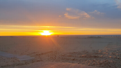 One person walking on a beach at sunrise.
