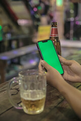 asian woman hands holding a mobile phone with chroma green screen at a vintage hippie bar