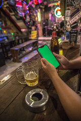 asian woman hands holding a mobile phone with chroma green screen at a vintage hippie bar