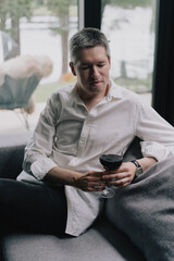 A man sitting on a couch holding glass of red wine in hand.