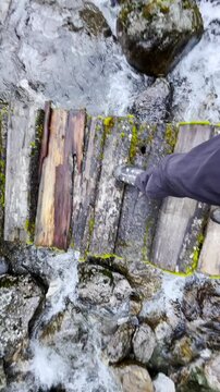 Slow motion 4K video POV view of Man's legs in trekking boots crossing mountain creek by wooden bridge during Makalu Barun National Park trek in Nepal. Mountain hiking and active people concept image.