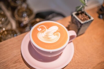 A close-up of a beautifully crafted latte art in a pink cup on a wooden table.