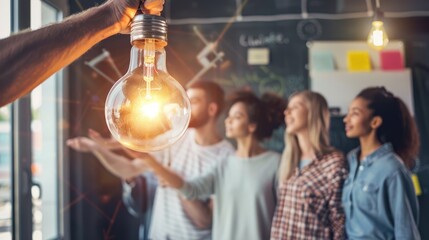 A group of young professionals are working together in an office. They are all looking at a light bulb that one of them is holding. The light bulb is glowing brightly. The people are all smiling and