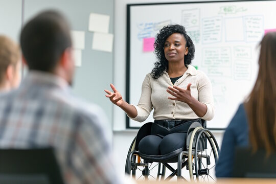 African American woman in wheelchair giving a presentation to colleagues. Office meeting, team discussion, workplace inclusion. Concept for leadership, teamwork, International Day of Persons with Disa