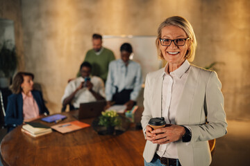 Senior businesswoman with coffee smiling at the camera at office on meeting