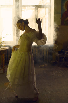 Young woman in a white dress dancing in a smoky room 