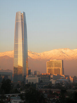 Sunset lights over Costanera building with snowy mountain range in the background and air pollution