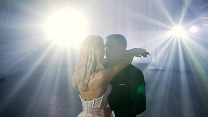 Fototapeta premium The bride and groom dance solo under bokeh lights during a wedding ceremony. Stylish groom and happy bride dance the first dance. A couple of bride and groom are dancing under the lights.