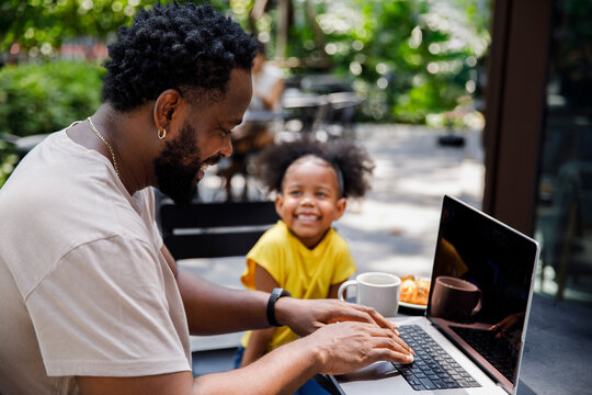 Happy daughter looking at father using laptop