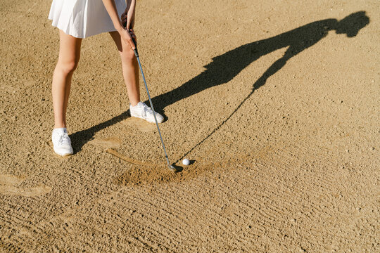  legs of young woman playing golf in the sun, her ball is a trap/ bun 