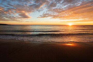 Waves rolling onto a beach at sunrise. Orange and yellow sky.