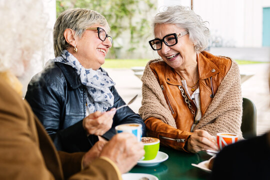 Senior women laughing while having breakfast with group of friends at cafeteria bar. Elderly lifestyle and friendship concept.