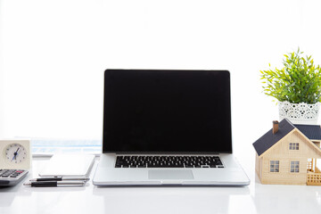 Fototapeta premium A laptop with a black screen on the table with a house model and a clock