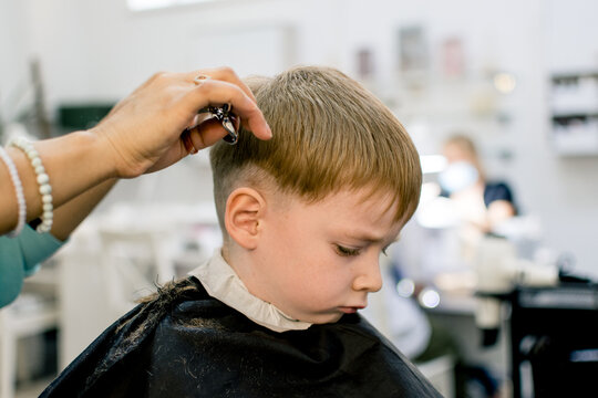 A little fair-haired boy is getting his hair cut in a barber shop.  