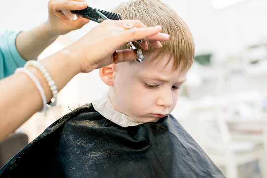A little fair-haired boy is getting his hair cut in a barber shop.  