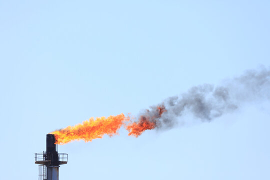 Tall stack with a flame / flare burning at the top. Oil refinery. 