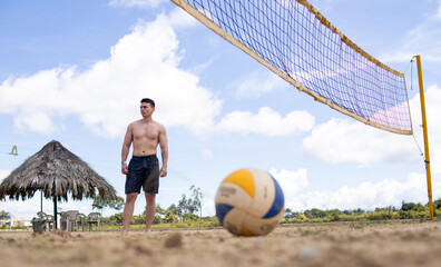 Shirtless young white man posing for the camera with a volleyball on a beach volleyball court