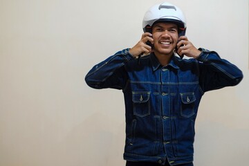 A Southeast Asian man wearing denim jacket and put white motorcycle helmet on head, showing smile, Positive person.