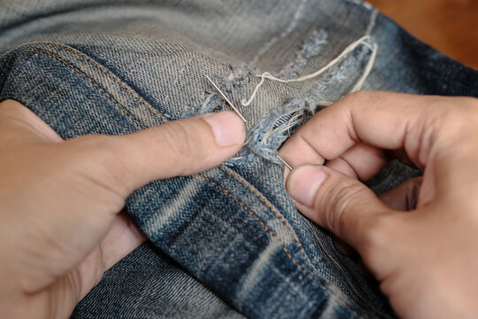 Jeans repair concept. A man sews up a hole in jeans. Sew a patch onto a hole in the knees. Top view, hand stitiching, garment industrial concept.