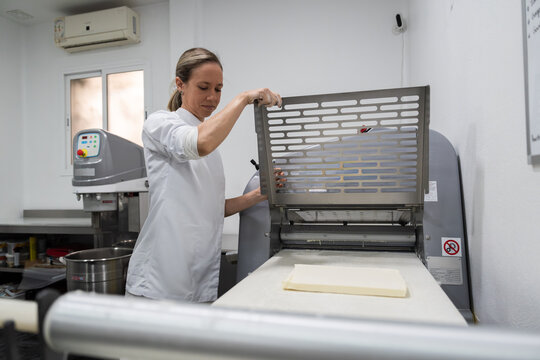 Female baker preparing dough with industrial roller machine