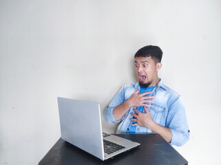 A man on his working place looking to laptop with shocked expression