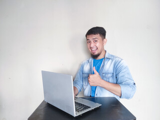 Adult Asian man smiling and give thumb up while working using laptop