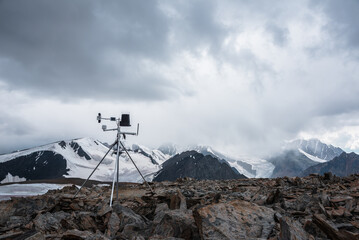 Automatic meteorological station on stone hill with view to large snow-capped mountain range....