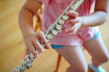 椅子に座ってフルートを吹いている小学5年生の女の子の手元。 © リリ