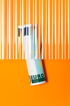 Euro banknote roll on orange background under corrugated glass 