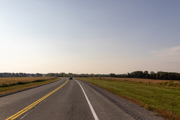 Fototapeta premium Open road ahead, bright sunshine - car journeying into distance - lush greenery on sides. Taken in Toronto, Canada.