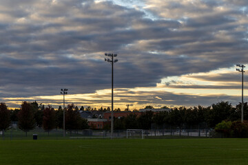 Sunset over soccer field - dramatic clouds - silhouette of stadium lights - trees behind. Taken in Toronto, Canada. © Jacob Tian