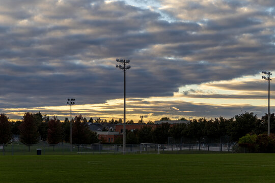 Sunset over soccer field - dramatic clouds - silhouette of stadium lights - trees behind. Taken in Toronto, Canada.