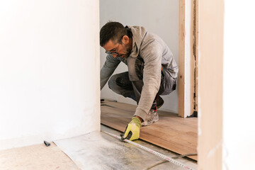 Focused carpenter measuring with tape on floor