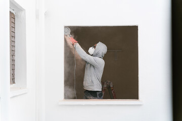 Focused contractor in hoodie using disc cutter on wall