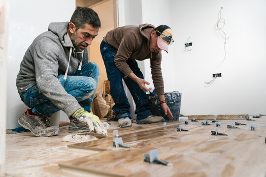 Focused tile layers installing laminate wood flooring in apartment