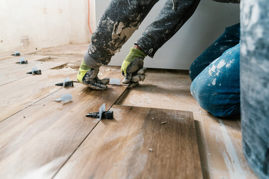 Unrecognizable tile layer installing wooden flooring in apartment