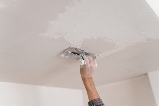 Crop male carpenter doing plaster with Trowel on roof at home