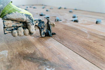 Hand of repairman laying wooden flooring with tile leveling system