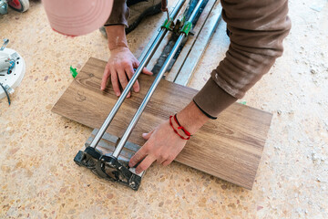 Crop handyman cutting wooden tile with cutter during flooring work