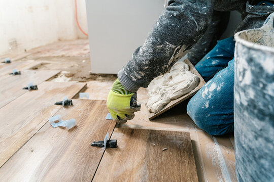 Crop workman installing wooden tile in room with adhesive material