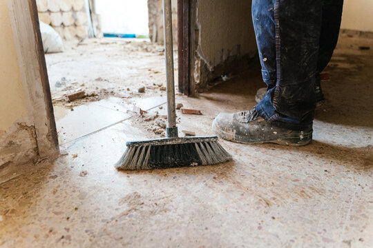 Anonymous handyman sweeping floor with broom in shabby room