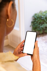 Holding smartphone, woman looking at blank screen in home setting, copy space
