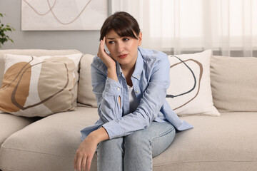 Upset woman suffering from headache on sofa at home