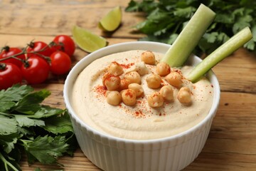 Tasty hummus with chickpeas in bowl and fresh products on wooden table, closeup