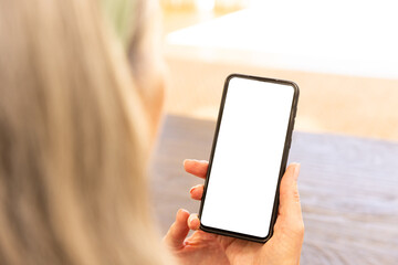 Holding smartphone, mature woman with blonde hair looking at blank screen, copy space
