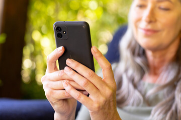 Using smartphone, mature woman smiling and relaxing at home