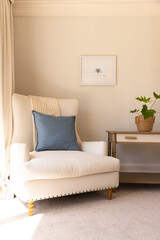 Cozy living room with white armchair, blue pillow, and potted plant on table, copy space