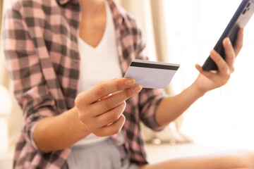 Holding credit card and smartphone, woman making online purchase at home