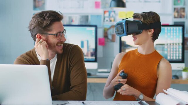 Female architect wearing virtual reality headset having fun and dancing next to male colleague at desk working on laptop - shot in slow motion